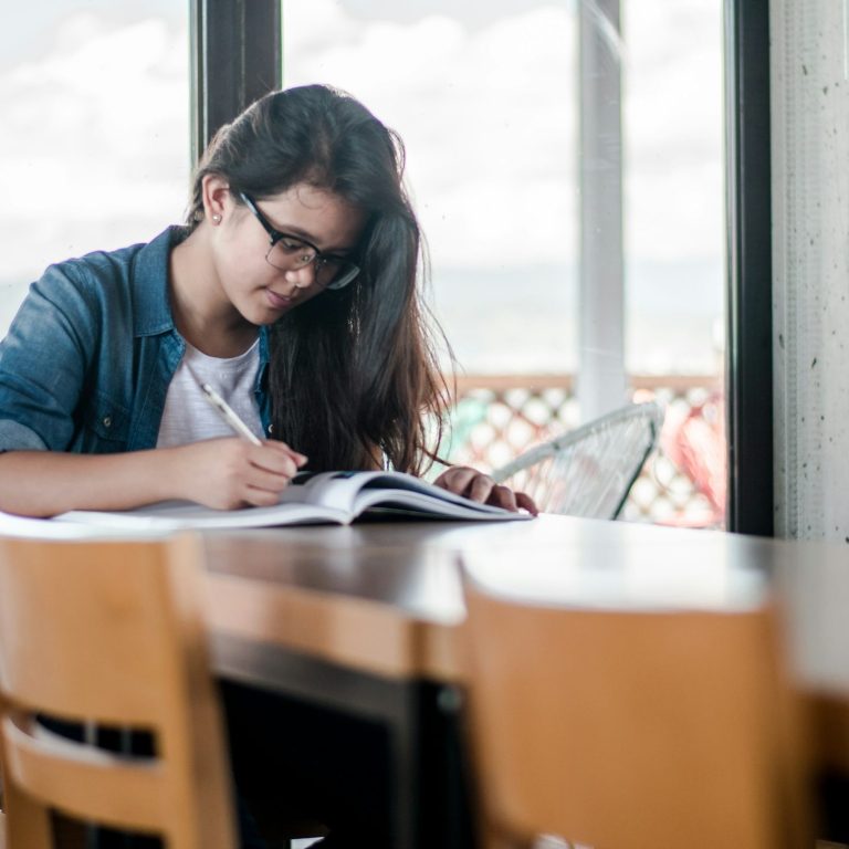 Young woman studying and writing in a notebook by a window