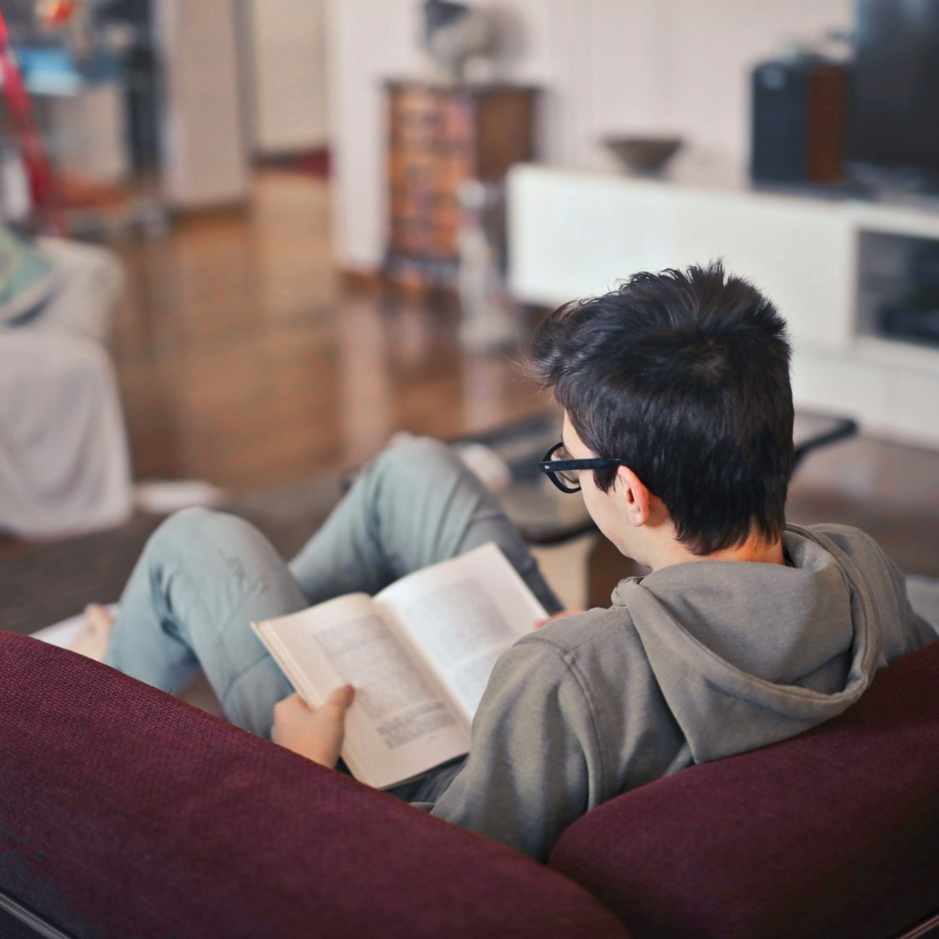 Young person relaxing and reading a book on a sofa at home
